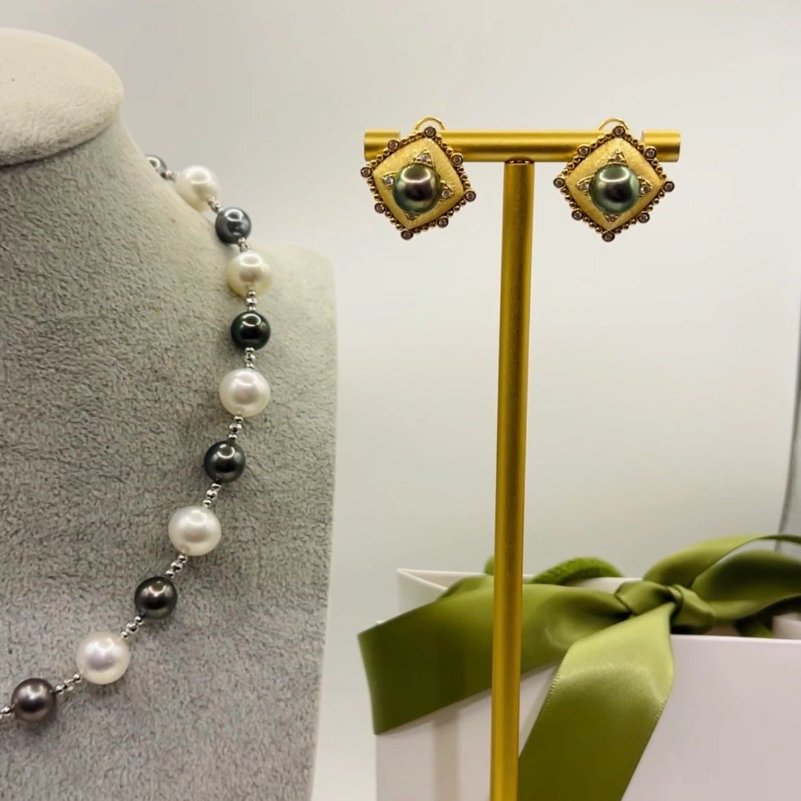 Elegant pearl necklace and gold earrings with dark pearls on display stand.