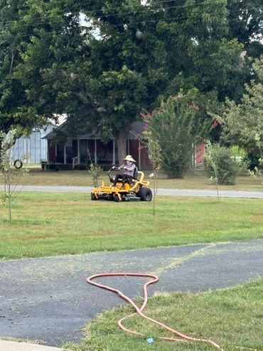 Person mowing lawn with a yellow riding mower on a sunny day.