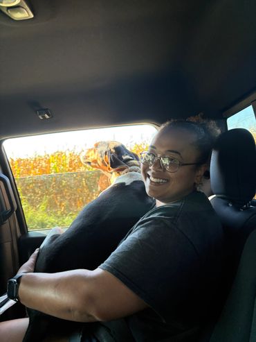 Woman happily holding a dog in a car seat with the window down.