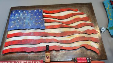 Rustic American flag wall art with hot sauce bottles below.