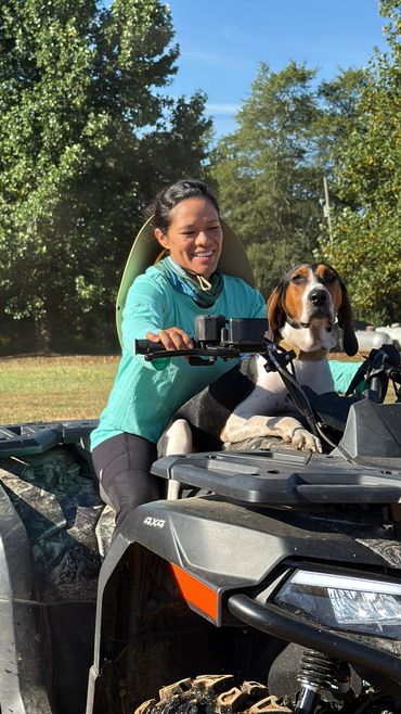 A woman and her dog ride an ATV together outdoors on a sunny day.
