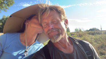 Woman kisses a smiling man outdoors on a sunny day.