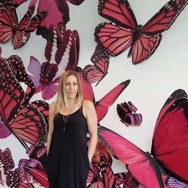 Artist and digital marketer Angie Clark standing in front of pink three dimensional butterfly wall