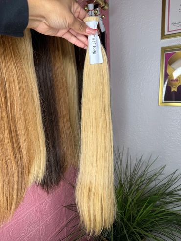 Hand holding a blonde hair extension labeled #22 100g among other hair extensions.