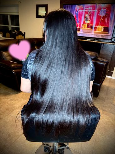 Person with long, shiny black hair seated on a stool in a living room.