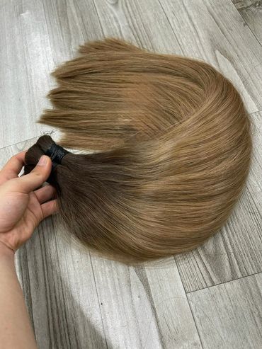Hand holding a bundle of two-toned hair extensions on a wooden floor.