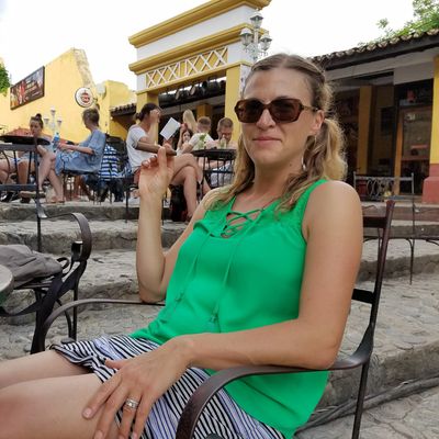 Woman in green top sitting outdoors with sunglasses.