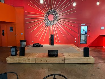 Small stage with speakers and sunburst wall art in a red room.