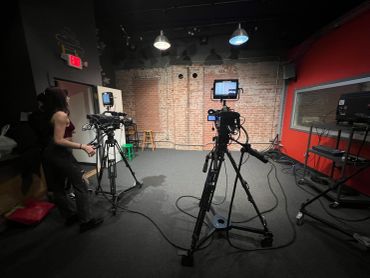 Two video cameras set up in a studio with a woman adjusting one of them.