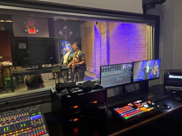 Music performance being filmed in a studio with control room equipment.