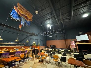 Empty event space with tables, chairs, and bar under dim lighting.