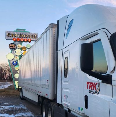 White semi-truck parked near Carlinville Plaza sign at sunset.