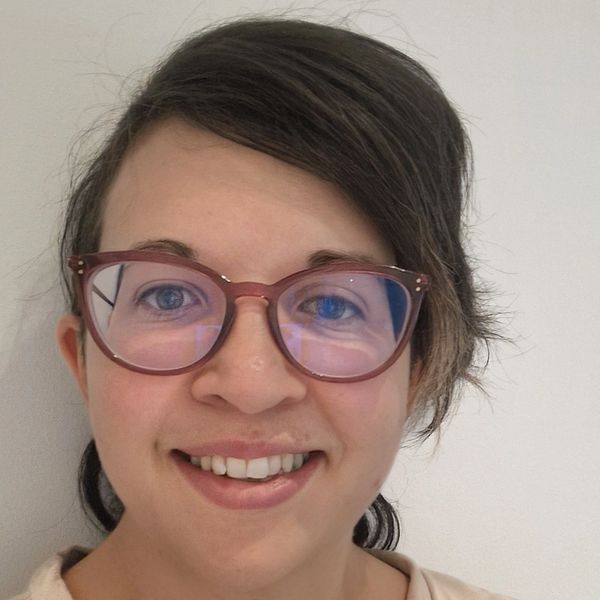 Front-on photograph of a Caucasian female, brown hair and pink glasses.