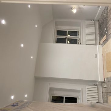 Empty room with white walls, ceiling lights, and windows.