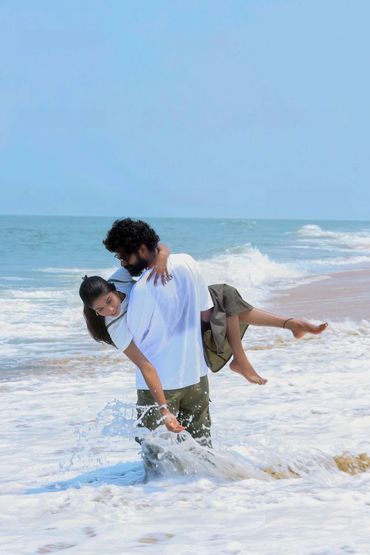 Couple enjoying playful moment at the beach with waves splashing around.