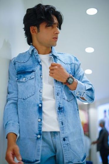 Young man in denim jacket and jeans looking sideways indoors.