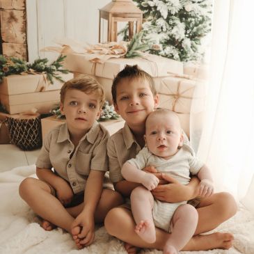 Three boys sitting together on a soft rug indoors.