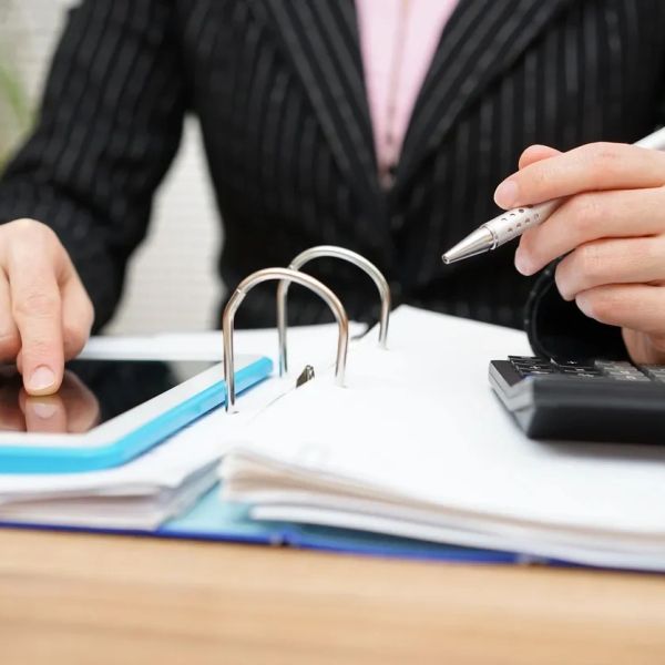 Person using tablet and calculator with documents on desk.