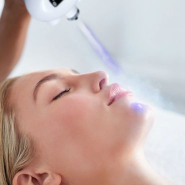 Woman receiving a facial skincare treatment with a device emitting blue light.