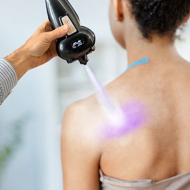 A device emits a purple light onto a woman's back for treatment.