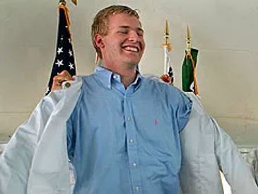 A smiling man putting on a white coat in front of flags.
