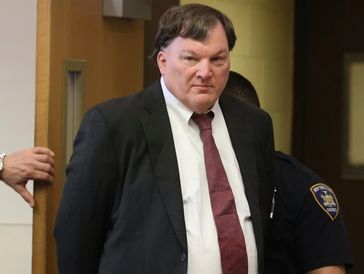 Man in a suit being escorted by a police officer in a hallway.