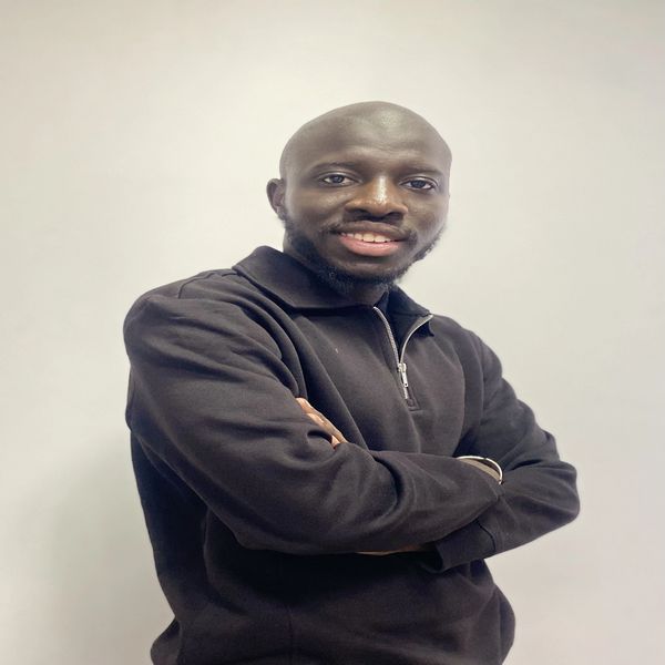 Confident man in a black zip-up sweater smiling with arms crossed against a plain background.