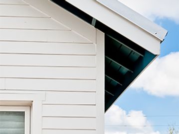 White house corner with siding and roof overhang under a blue sky.