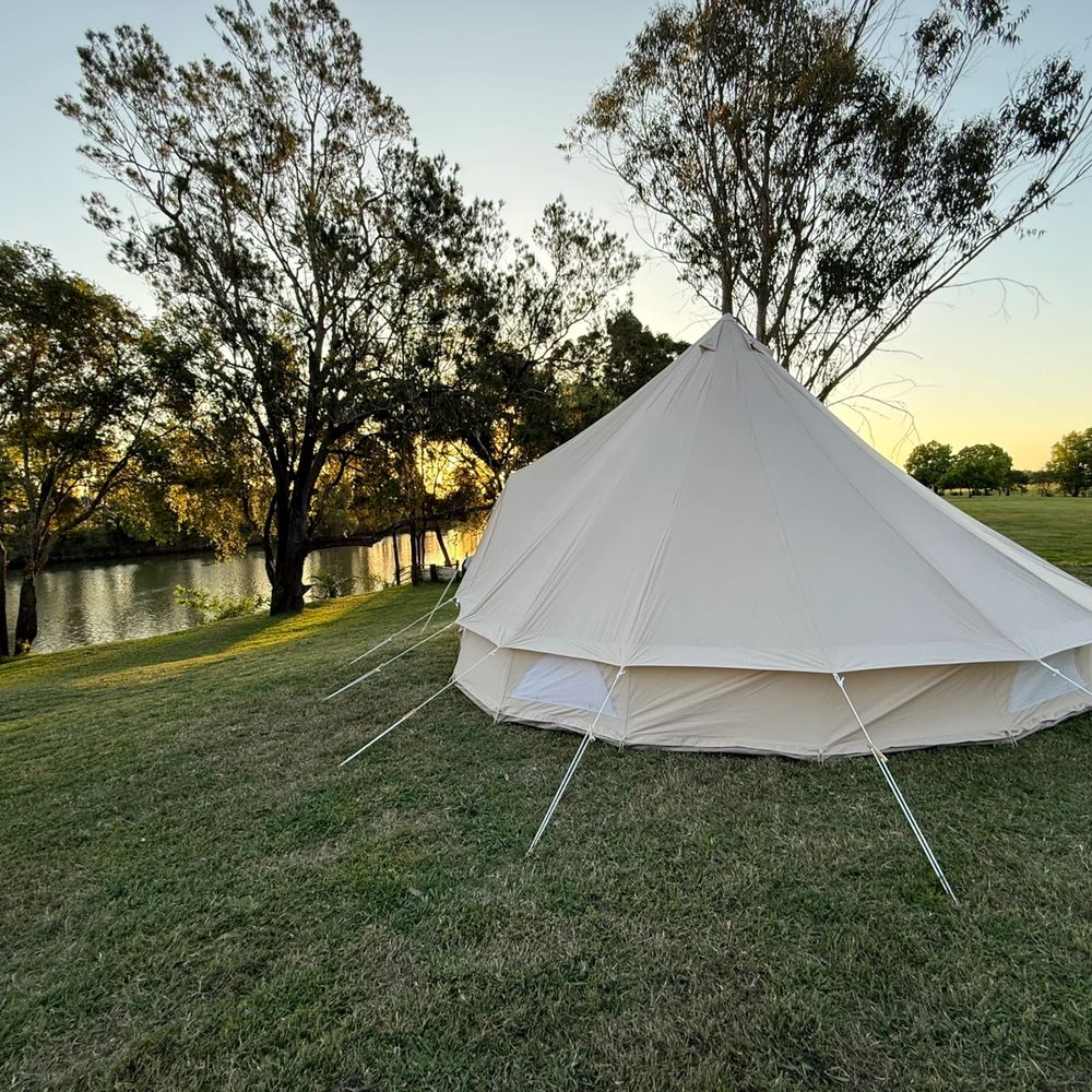 A cream-colored tent set up on a grassy field near a river at sunset.