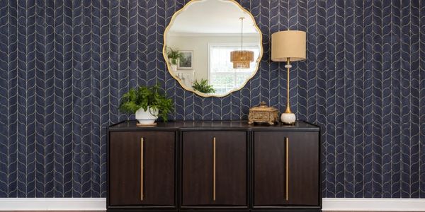 Dark wooden cabinet with gold handles under a decorative round mirror.