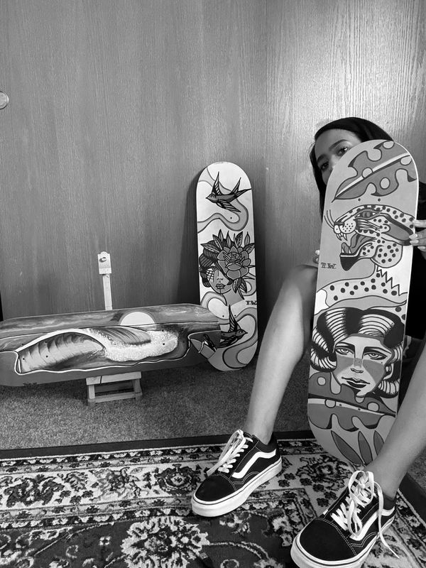 Woman showcasing three artistic skateboard decks with vibrant, detailed designs indoors.
