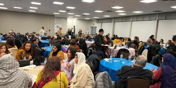Large indoor gathering with people seated at round tables.