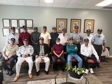 Group of elderly men wearing caps sitting and standing indoors.