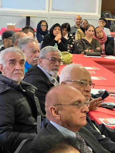 A group of elderly people attend a meeting, listening intently.