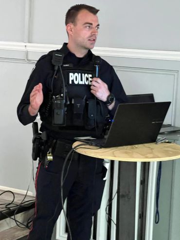 Police officer speaking with a microphone beside a laptop.