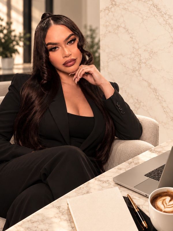 Confident woman in black suit sitting in an office setting.