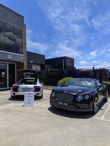 Luxury cars Audi R8 and Bentley parked under a bright blue sky.