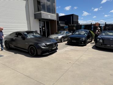A lineup of luxury cars parked outside a building under a sunny sky.