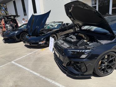 Three black sports cars with open hoods displayed outdoors at a car event.