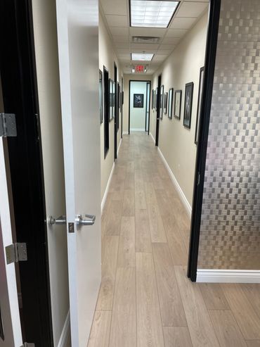 Long hallway with open door, artwork on walls, and wooden floor.
