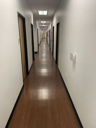 Long, narrow hallway with wooden floors and white walls featuring multiple closed doors.