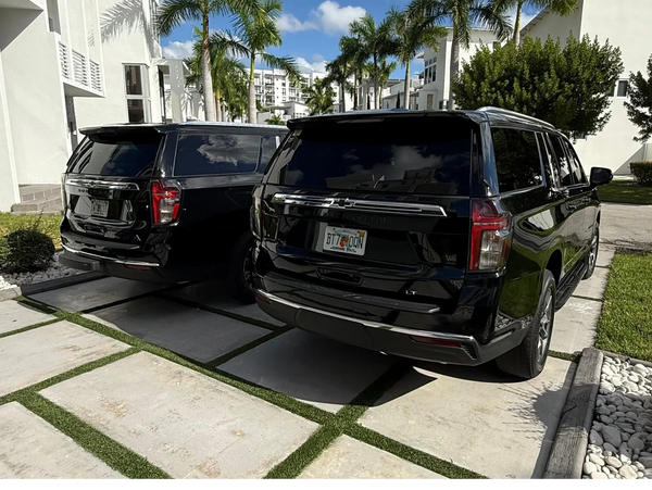 Two black SUVs parked in a sunny, palm-tree-lined residential area.
