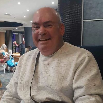 Smiling man sitting at a restaurant table with a drink.