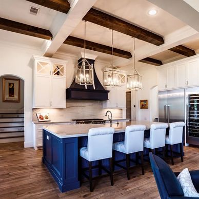 Elegant kitchen with blue island, white cabinetry, and wooden ceiling beams.