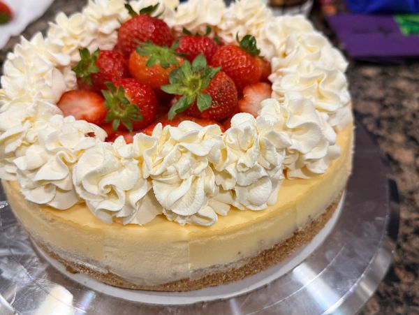 A cheesecake topped with whipped cream and fresh strawberries.