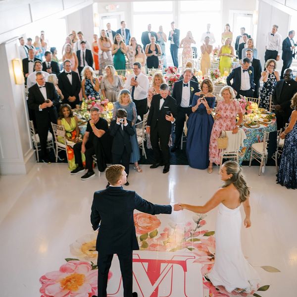 Bride and groom hold hands during their wedding dance in front of an audience.