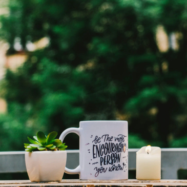 A motivational mug, plant, and candle on a wooden surface.