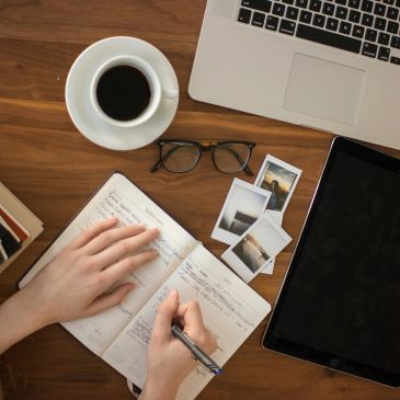 Person writing in a planner with coffee and laptop nearby.