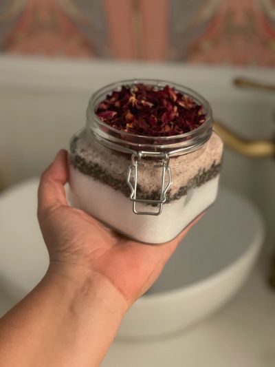 Hand holding a jar with layers and dried rose petals.