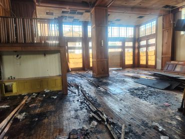 Interior of a fire-damaged room with debris and soot on wooden floors.
